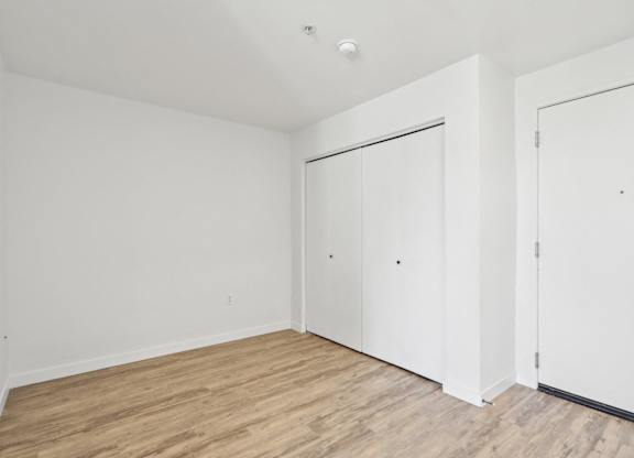 A room with white walls and wooden flooring with two doors.