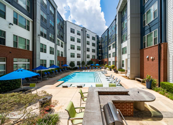 an outdoor pool with lounge chairs and umbrellas in front of an apartment building