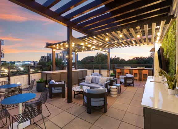 a rooftop patio with tables and chairs and a pergola at dusk