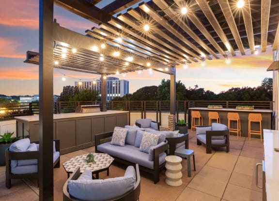 a roof deck with couches and chairs and a bar with a sunset