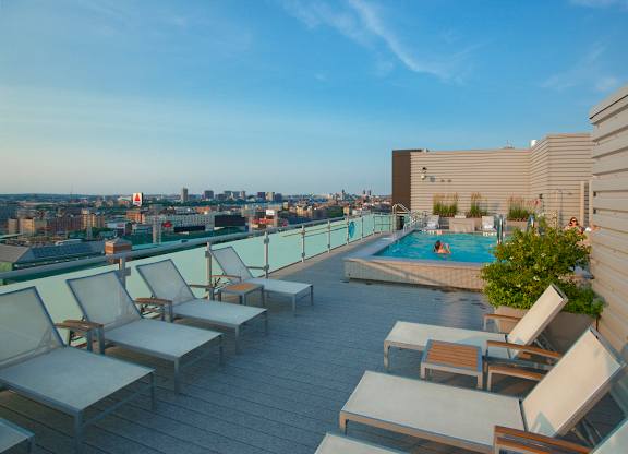 A rooftop patio with chairs and a pool overlooking a city skyline.