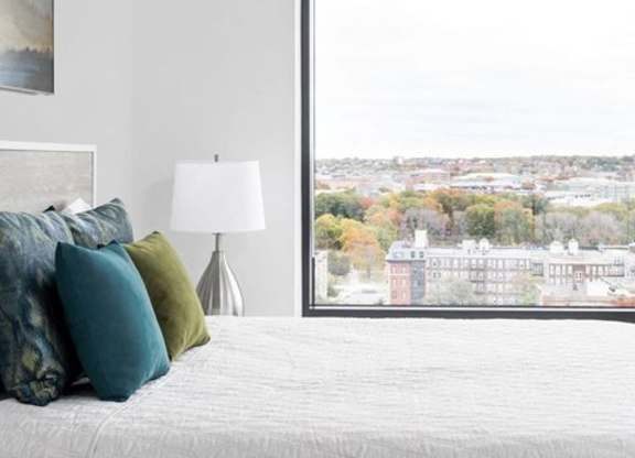 A bedroom with a large bed and a view of a cityscape through a window.