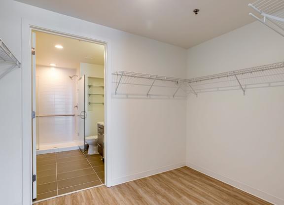 A white room with a walk-in closet and a bathroom visible through the door.