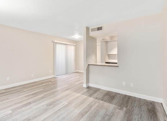 A room with light wood flooring and a window with blinds.