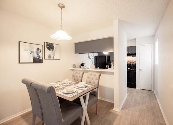 A dining room with a table set for two and a kitchen in the background.