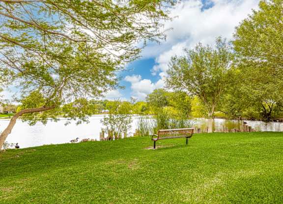 A park bench sits on a grassy hill overlooking a lake.