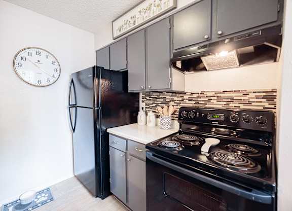A black refrigerator is in a kitchen next to a stove.