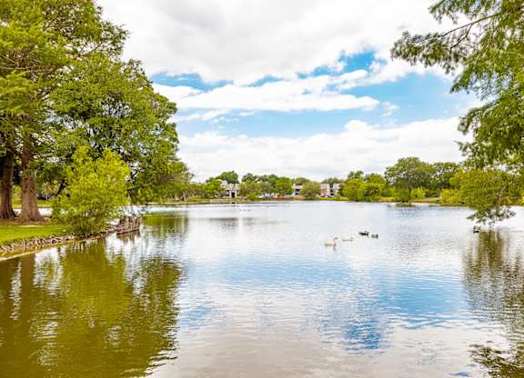 A serene lake surrounded by lush green trees under a partly cloudy sky.