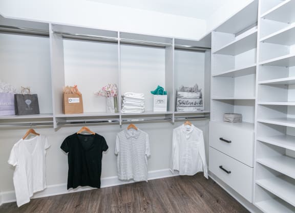 a walk in closet with white shelves and a window