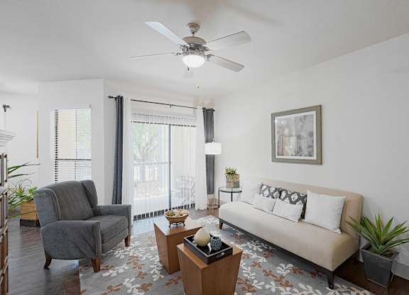 A living room with a grey couch, a grey armchair, a coffee table, a potted plant, and a framed picture on the wall.