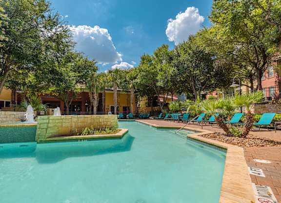 A swimming pool surrounded by trees and lounge chairs.