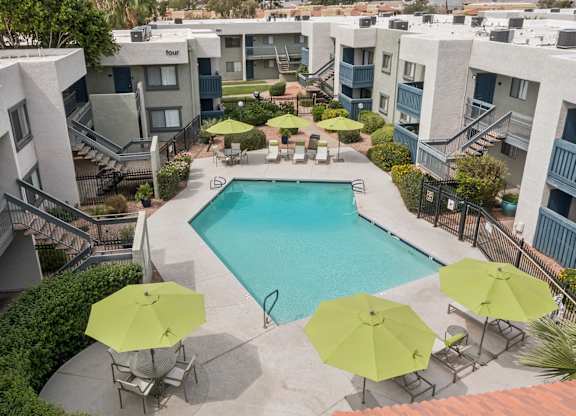 A pool surrounded by chairs and umbrellas in a courtyard.