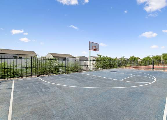 A basketball court with a red hoop and a black fence.