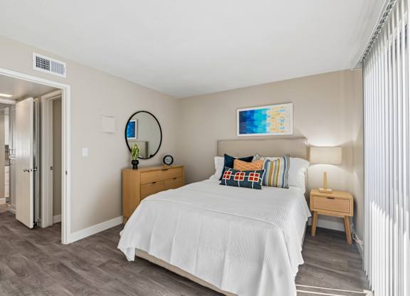 A bedroom with a bed, nightstand, and a mirror on the wall.