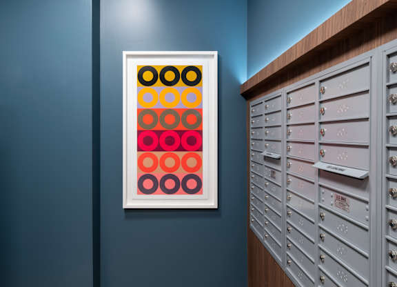 A framed picture of circles in different colors is hanging on a wall next to a row of mailboxes.