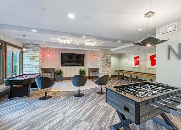 A foosball table is in the middle of a room with a pool table and a couch.
