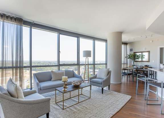 A living room with a grey couch, a grey armchair, a coffee table and a large window with a view of the beach.