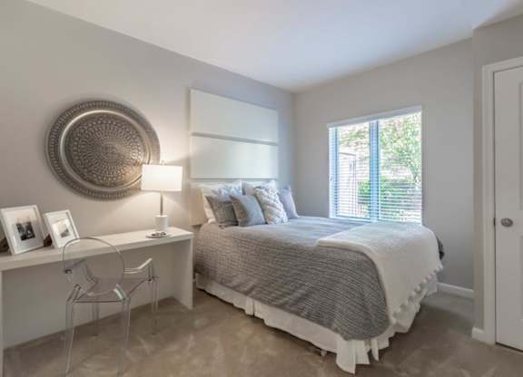 A bedroom with a bed, desk, chair, and window.