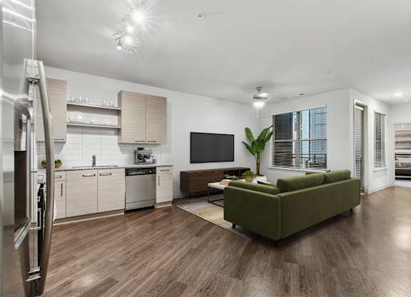 A modern kitchen with a refrigerator on the left and a green couch in the middle of the room.