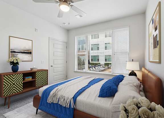 A bedroom with a bed, a fan, a vase of flowers, and a picture on the wall.