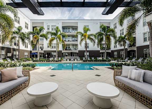 A pool surrounded by palm trees and white furniture.