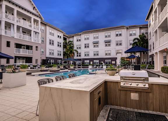 A poolside grill is in front of a pool and apartment buildings.