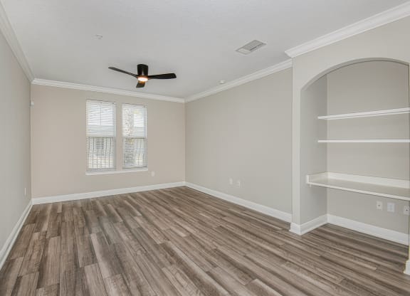 an empty bedroom with a ceiling fan and shelves