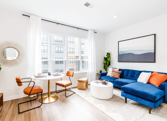 a living room with a blue couch and a round table and a large window at One Ten Apartments, New Jersey