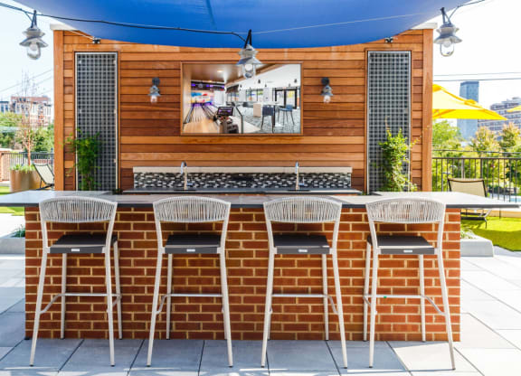 the outdoor bar is under a blue awning and a brick wall with chairs at One Ten Apartments, Jersey City , New Jersey