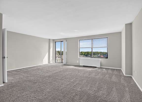 A spacious room with grey carpeting and a large window.