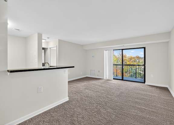 A spacious room with a carpeted floor and a sliding glass door leading to a balcony.