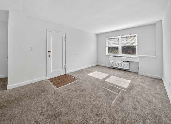 A room with a carpet, a door, a window with a view of trees and a small table.