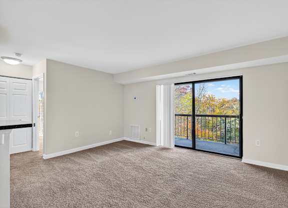 A spacious room with a carpeted floor and a sliding glass door leading to a balcony.