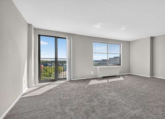 A spacious room with grey carpeting and large windows overlooking a parking lot.