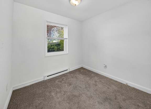 A room with a carpeted floor and a window showing a view of trees and a house.