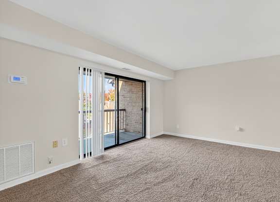 A room with a carpeted floor and a sliding glass door leading to a balcony.