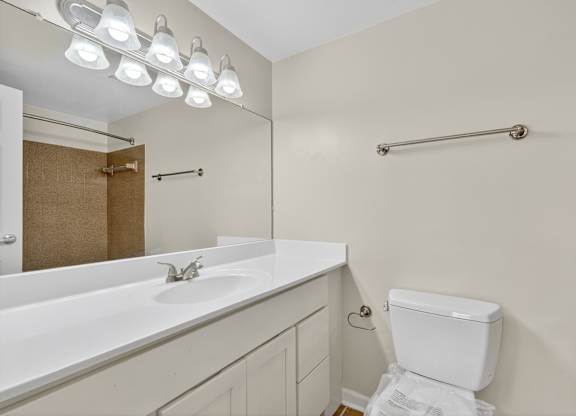 A white toilet sits in a bathroom with a white sink and mirror.