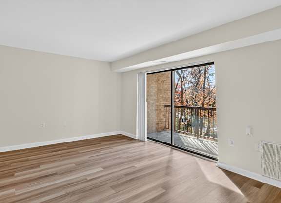 A room with wooden flooring and a sliding glass door leading to a balcony.