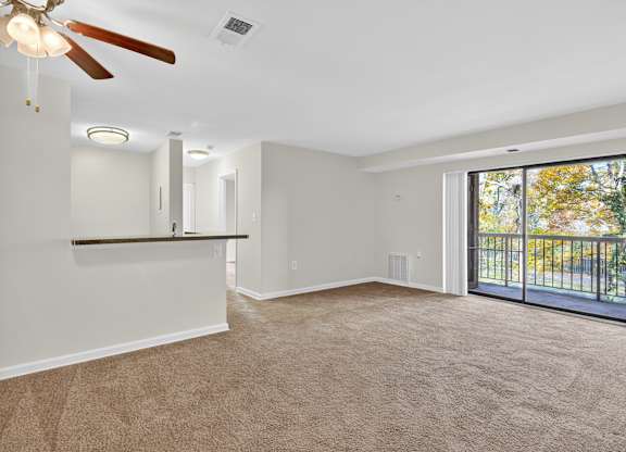 A spacious room with a ceiling fan and sliding glass doors leading to a balcony.