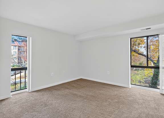A room with a carpeted floor and two open doors leading to balconies.