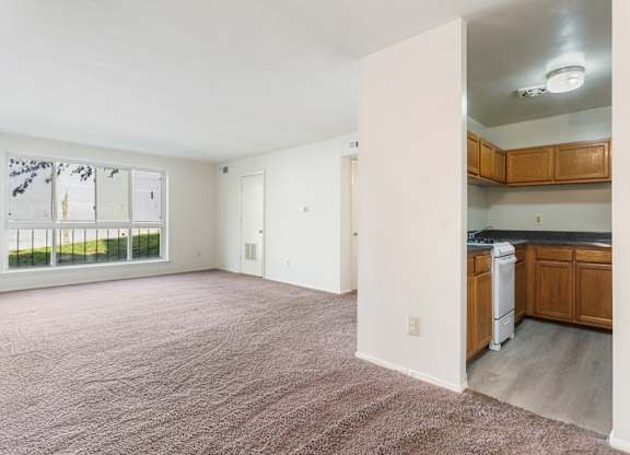 A large, empty room with a kitchen area visible through the open door.