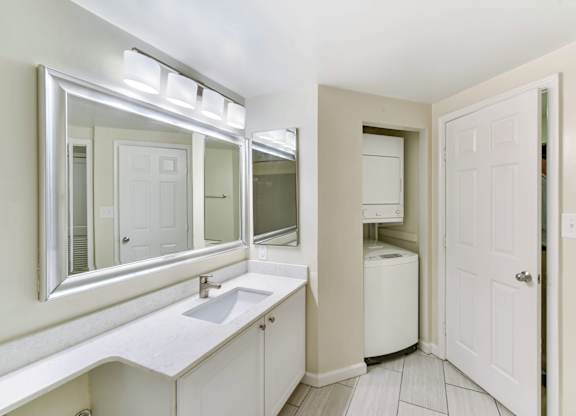 A white bathroom with a sink, mirror, and a white door.