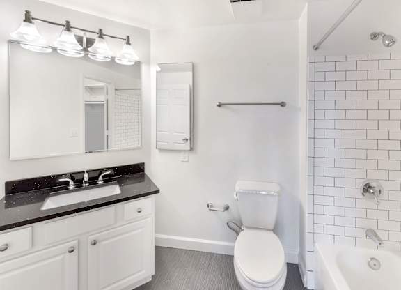 A white toilet sits in a bathroom next to a sink and a bathtub.