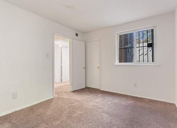 A room with a carpeted floor and a window with bars on it.