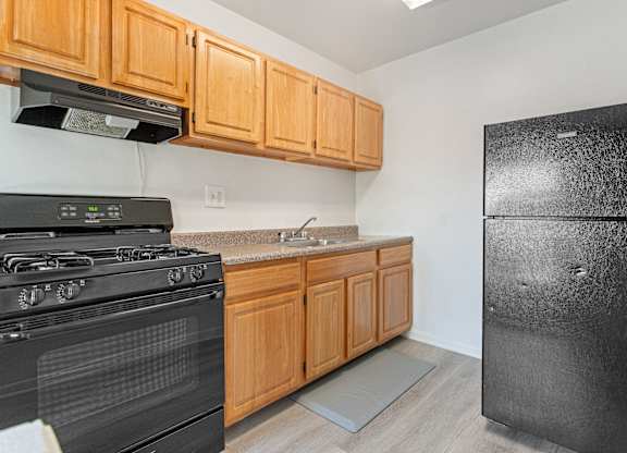 A black stove and refrigerator in a kitchen with wooden cabinets.