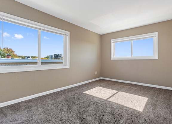 A room with a carpeted floor and two windows.