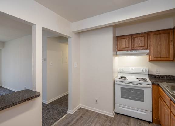 A kitchen with a white stove top oven and wooden cabinets.