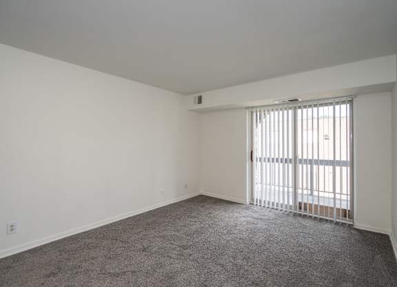 A room with a carpeted floor and a window with blinds.