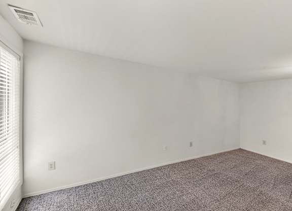 A room with white walls and a window with blinds.