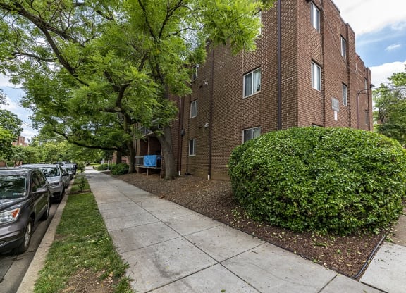 a brick apartment building with a sidewalk and trees